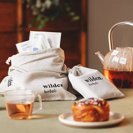 Wilden Herbals tea bags, a glass teapot of herbal tea and a cinnamon roll