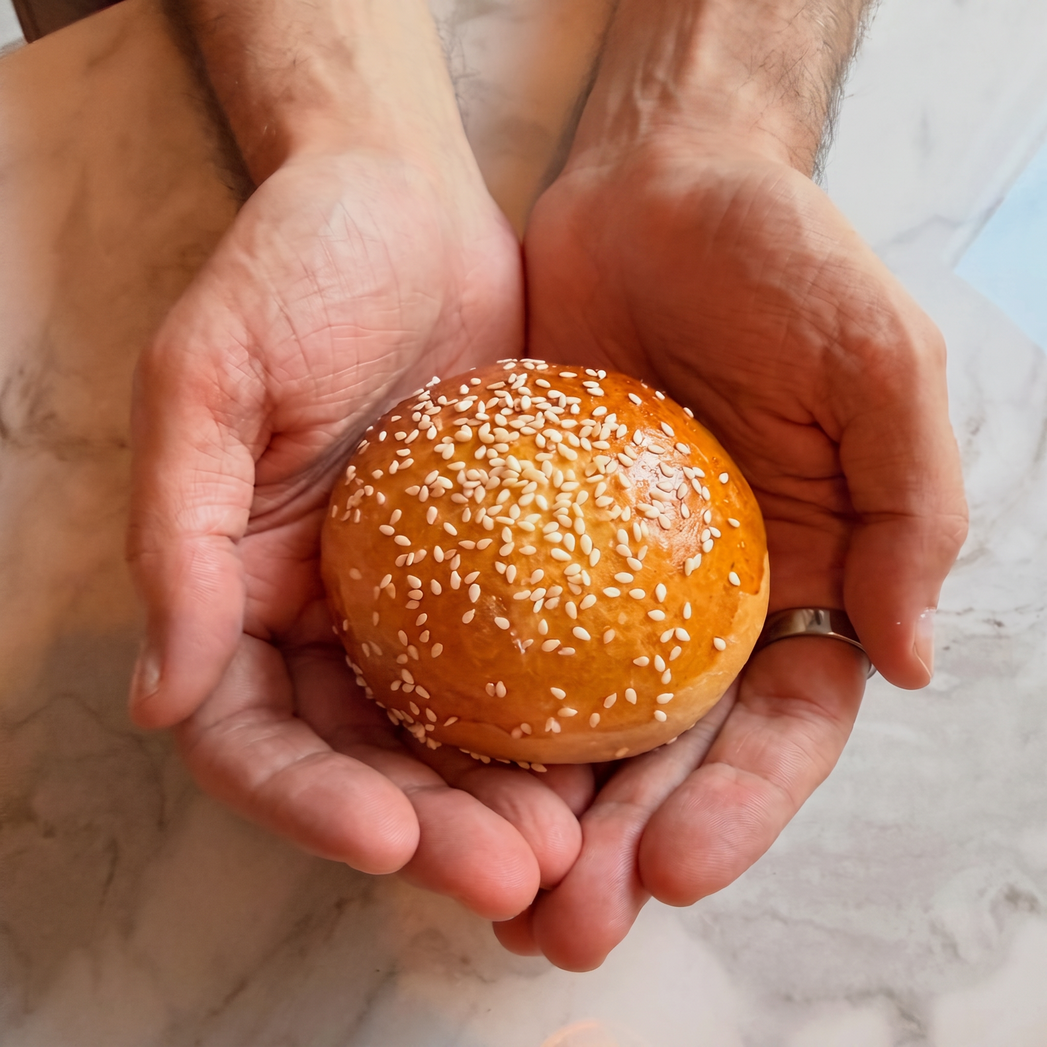 Hands cradling a freshly baked sesame-topped bun